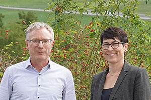 A man and a woman in front of a green landscape.