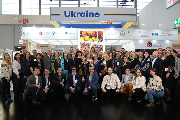 A group of about 50 people in front of a Ukraine stand. 