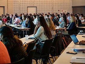 People at tables watching a workshop.