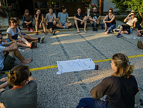 Eine Gruppe von Menschen sitzt im Kreis auf dem Boden.