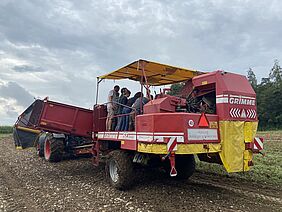 Eine grosse landwirtschaftliche Maschine mit mehreren Menschen drauf auf einem Feld.