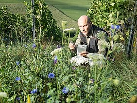 A man squatting in a meadow.
