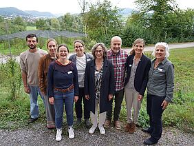 Acht Menschen stehen vor Naturhintergrund.